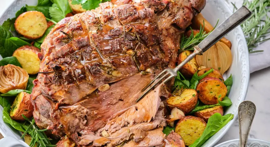 En saftig lammstek med ben, omgiven av rostade potatisar, lök och färska örter. Perfekt för en festlig middag.