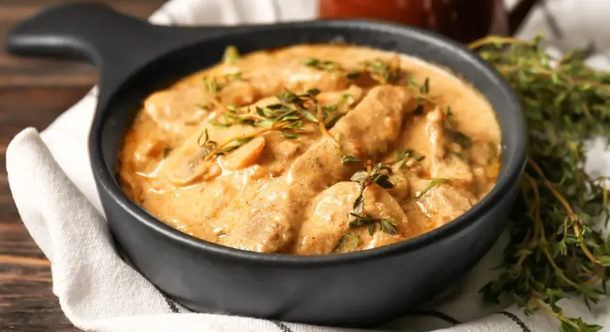 Cremiges Rindfleisch mit Pilzen, garniert mit frischem Thymian. Ein köstliches stroganoff rezept original, serviert in einer schwarzen Schüssel.
