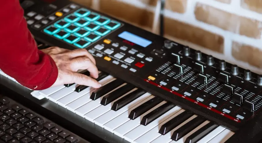 Hand spielt auf einem Keyboard, das für die Erzeugung von Synth-Musik verwendet wird. Viele Knöpfe und Pads sind sichtbar.