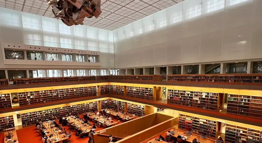 Große Bibliothek mit vielen Regalen voller Bücher. Menschen sitzen an Tischen und lesen. Ein Ort für Lesungen in Berlin.