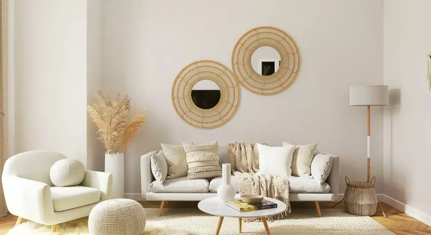 Salón acogedor con butaca blanca y sofá gris, decorado con espejos de mimbre y plantas secas. La combinación de sofá y butaca crea un espacio perfecto para relajarse.