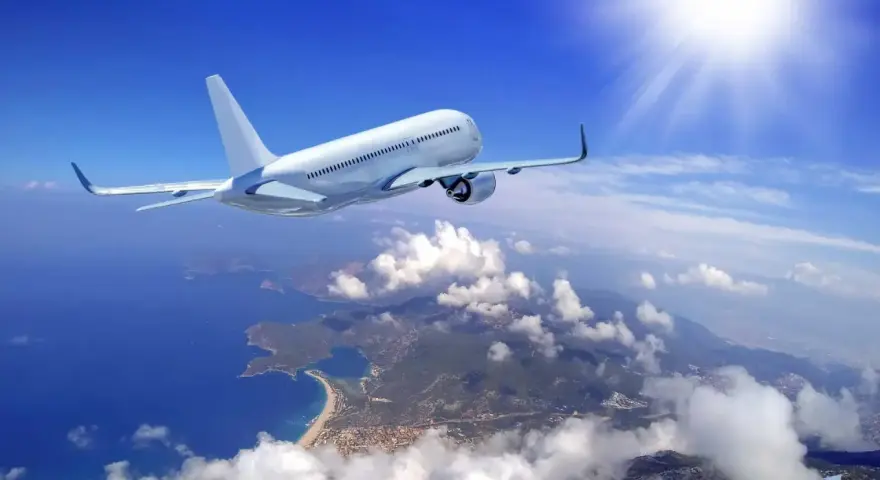 Un aereo bianco solca il cielo azzurro sopra una costa frastagliata. Il sole splende, creando un senso di distacco del vitreo e aereo.