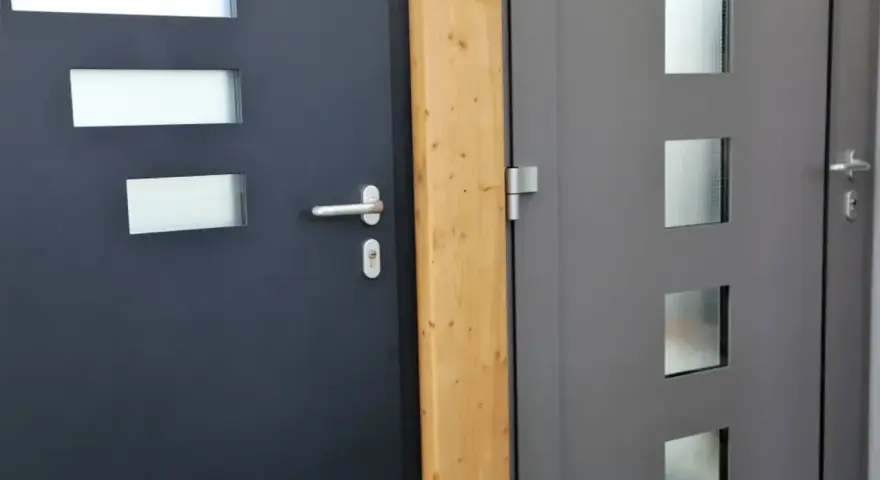 Dwie nowoczesne drzwi wejściowe, jedna ciemnoszara z prostokątnymi przeszkleniami, druga szara z kwadratowymi. Dowiedz się, jak uszczelnić drzwi wejściowe.