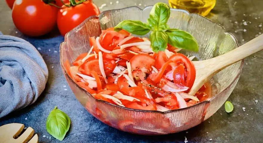 Frischer tomatensalat mit zwiebeln, garniert mit Basilikum. Daneben liegen frische Tomaten und ein Holzlöffel.