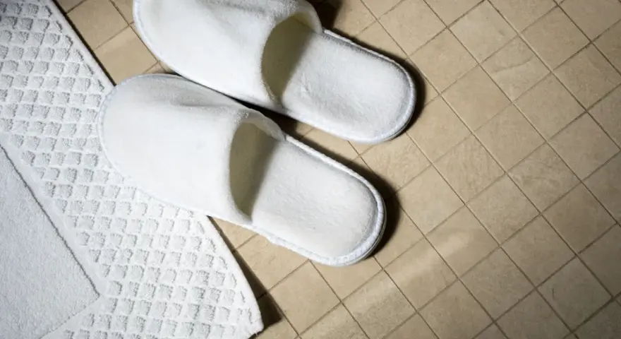 Białe hotelowe kapcie na kafelkach. Zastanawiasz się, czy można zabrać kapcie z hotelu?