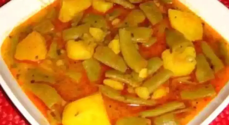 Un plato humeante de judías verdes con patatas, cocinado en una sabrosa salsa rojiza.