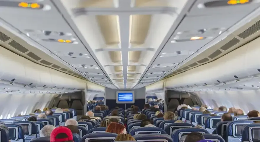 Wnętrze samolotu Boeing 737 Ryanair. Pasażerowie siedzą w rzędach niebieskich foteli, patrząc w stronę kokpitu.