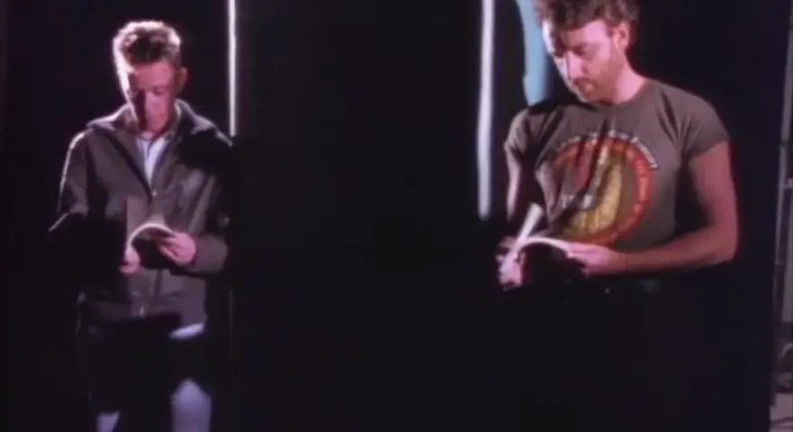 Dwóch mężczyzn czyta. Jeden w kurtce, drugi w koszulce z napisem. Atmosfera jak z "Blue Monday" New Order.