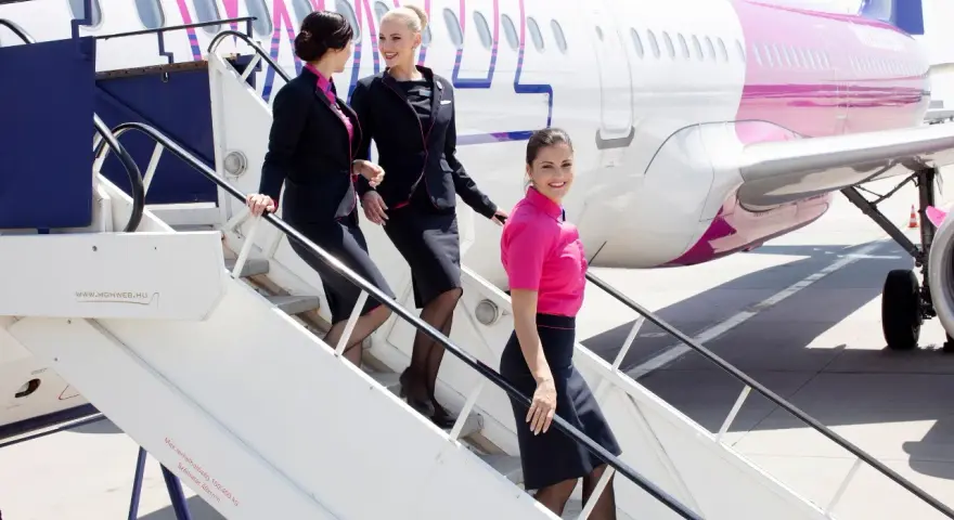 Uśmiechnięte stewardessy Wizz Air schodzą po schodkach. Ciekawe, ile zarabia stewardessa Wizz Air za taką pracę?