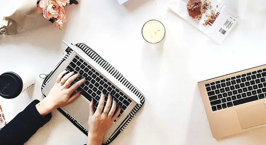 Kobieta pisze na laptopie, przygotowując wypowiedzenie umowy o dzieło. Obok świeca, muffinka i bukiet kwiatów.