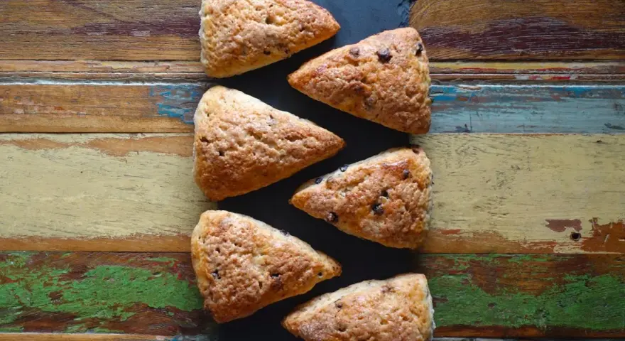 Sechs dreieckige Schokoladen-Scones liegen auf einem rustikalen Holztisch. Perfekt für alle, die keine komplizierten discard rezepte mögen.