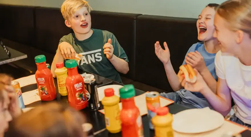 Barn skrattar och äter korv med bröd vid ett bord med Felix ketchup och senap. Perfekt för tips på femkamp!