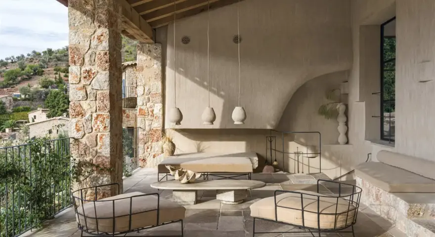 Acogedora terraza interior piso con sillones de metal, sofá y mesa de centro de piedra, bajo un techo de madera y rodeada de muros de piedra.