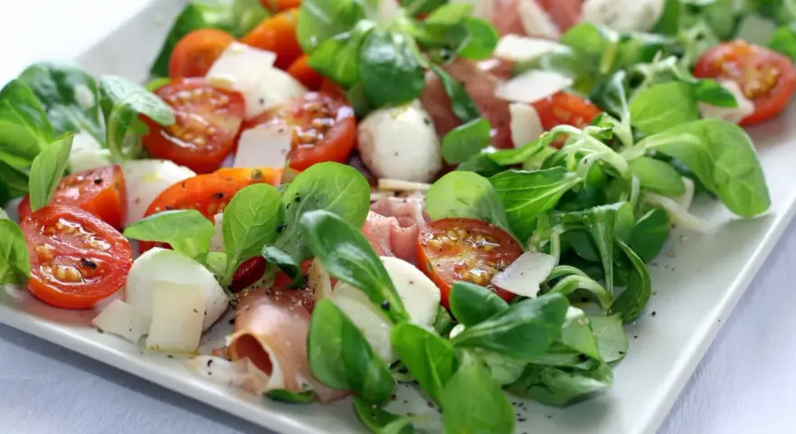 Pyszna sałatka z szynką parmeńską, pomidorkami koktajlowymi, mozzarellą i świeżą rukolą. Idealna na lekki posiłek.