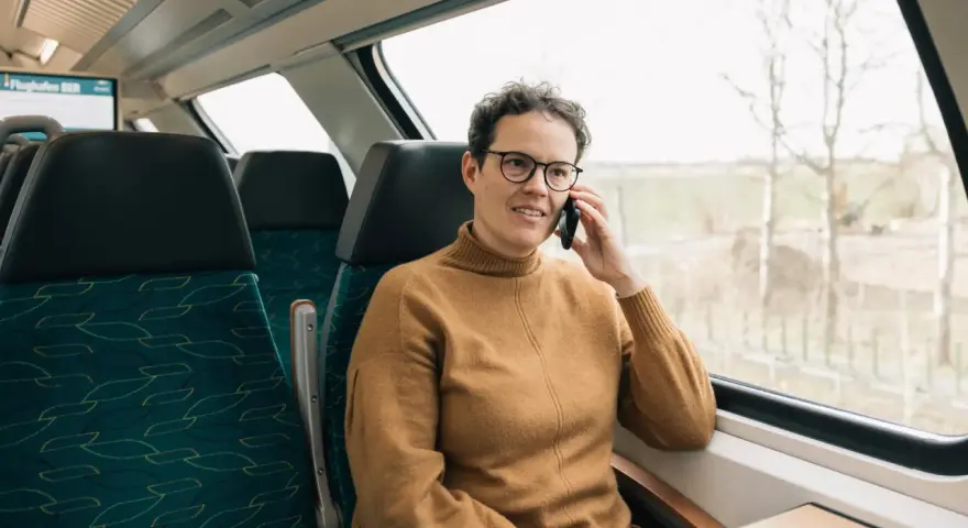 Kobieta w brązowym swetrze rozmawia przez telefon w pociągu. Czas na moją kolej, by usiąść przy oknie i podziwiać widoki.
