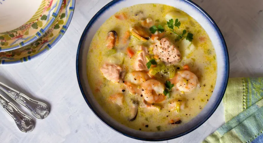 Sopa cremosa de pescado con salmón, gambas y mejillones, decorada con perejil.