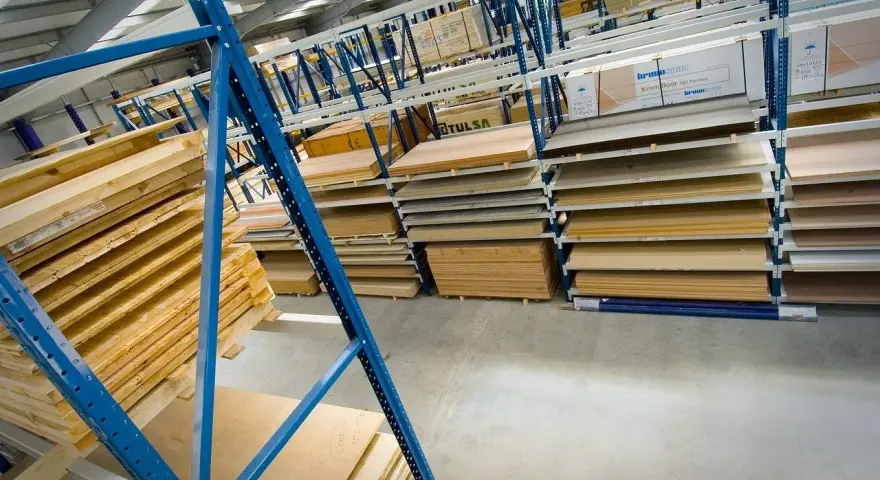 Magazyn pełen płyt, w tym **hdf**, drewnianych desek i materiałów budowlanych, ułożonych na niebieskich regałach.