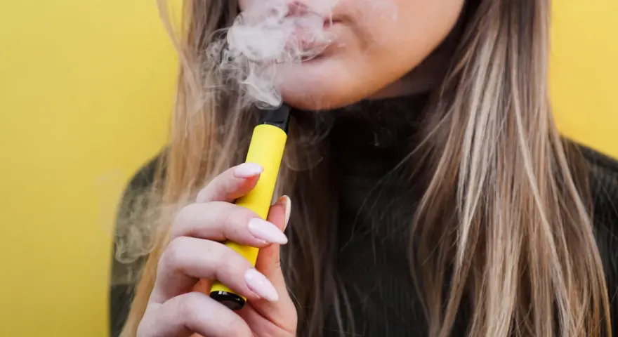 Mujer exhala vapor de un vaper sin nicotina, pero ¿sabías que el vaper sin nicotina mancha los dientes?