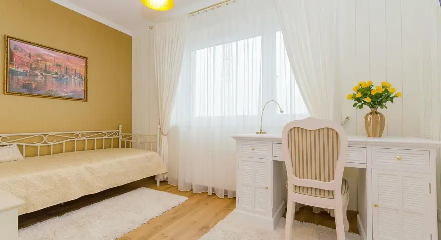 Dormitorio con paredes doradas, cama blanca y escritorio. Los colores que combinan con el amarillo en paredes son el blanco y los tonos tierra, creando un ambiente cálido y luminoso.