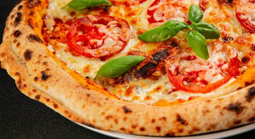 Pyszna pizza Margherita z pomidorami i bazylią, idealnie wypieczona w wysokiej temperaturze przez kilka minut.