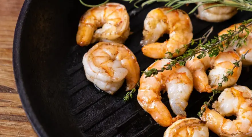 Gambas a la plancha jugosas y doradas, con ramitas de tomillo fresco sobre una sartén de hierro fundido.
