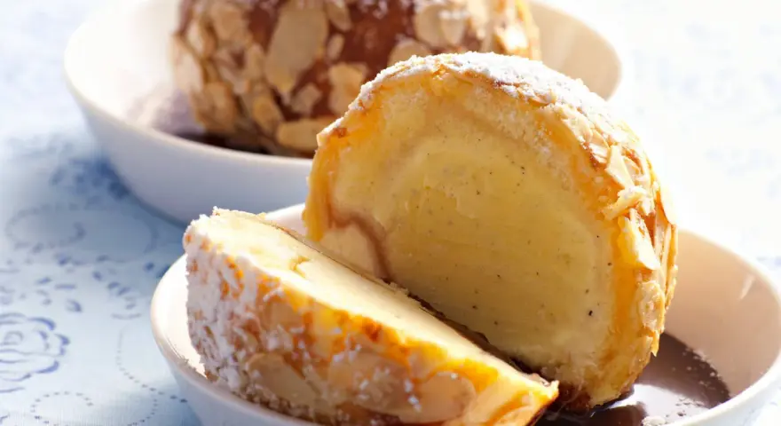 Zwei Portionen gebratenes Eis, umhüllt von Mandelsplittern und mit Puderzucker bestäubt, serviert in weißen Schalen.
