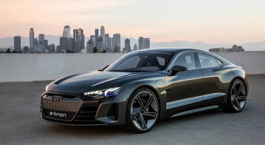 Ciemnoszary Audi e-tron GT stoi na tle panoramy miasta o zachodzie słońca.
