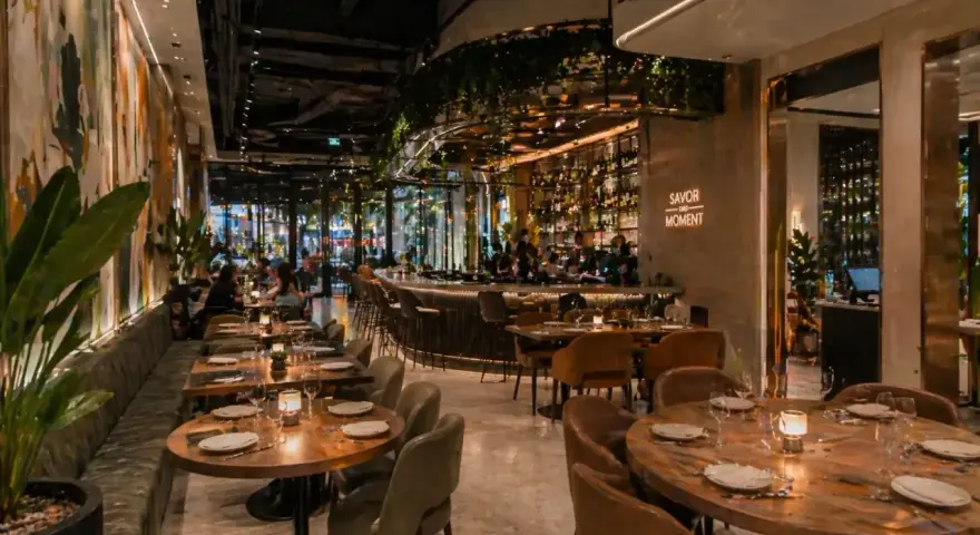 Elegantes mesas y un bar iluminado, con arte mural y plantas, ofrecen **ideas decoración restaurante** acogedoras.
