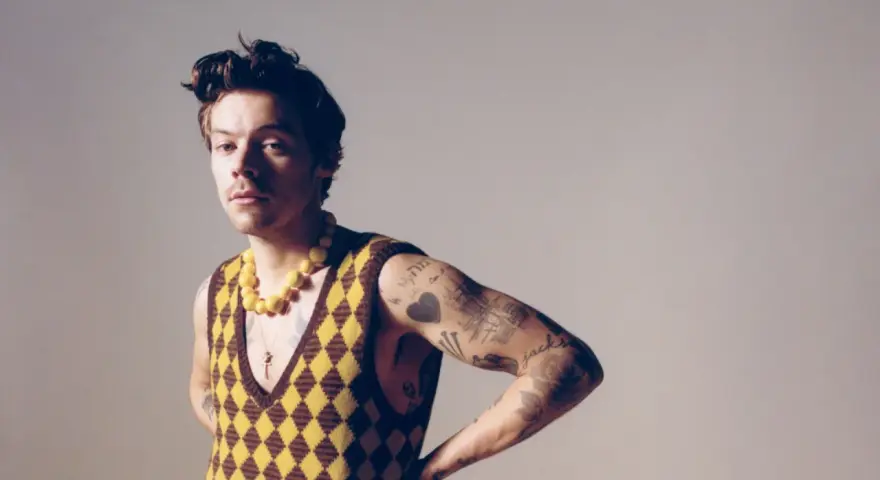 Harry Styles w kamizelce w romby i żółtym naszyjniku, jakby inspirował nowe harry styles utwory.