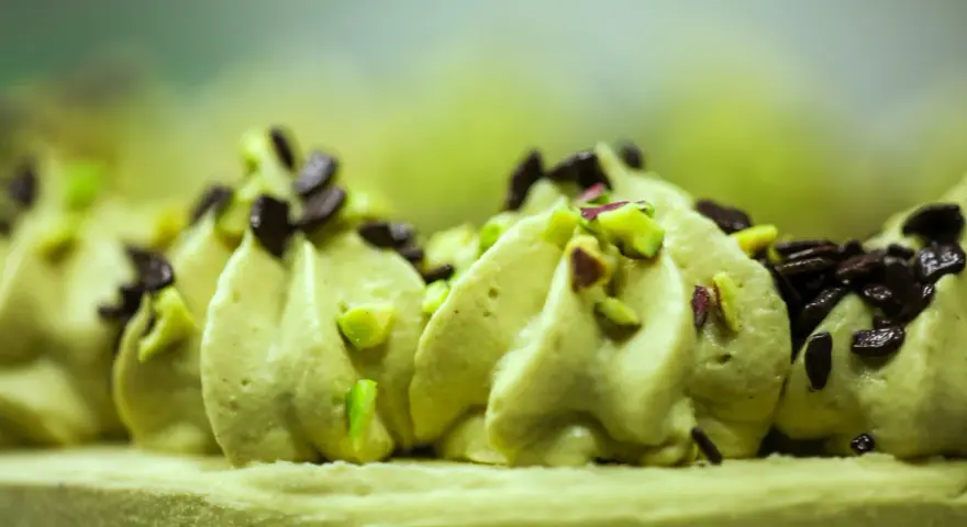 Delikatna masa pistacjowa ozdobiona kawałkami pistacji i czekolady, tworząca apetyczny deser.