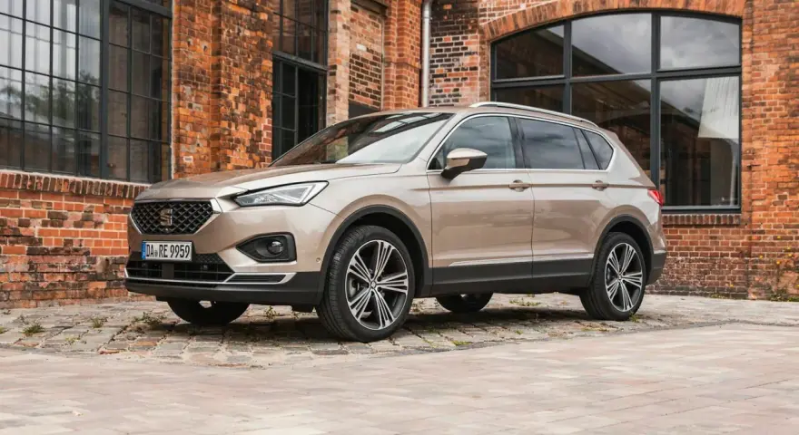 Beiger Seat Tarraco vor Backsteinhaus. Keine Seat Tarraco Probleme hier, nur stilvolles Fahren.