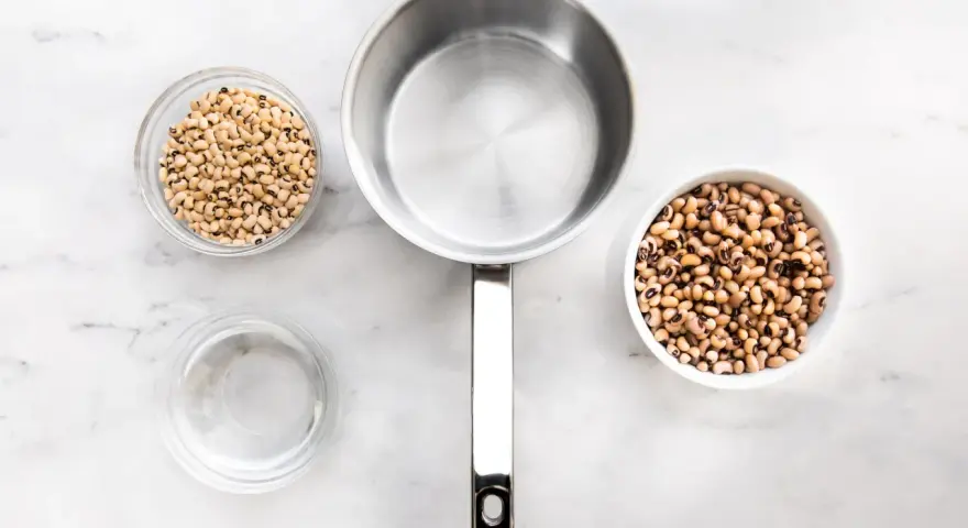 Vorbereitung zum Bohne kochen: zwei Schüsseln mit Schwarzaugenbohnen, ein Topf und eine Schüssel Wasser auf Marmoruntergrund.