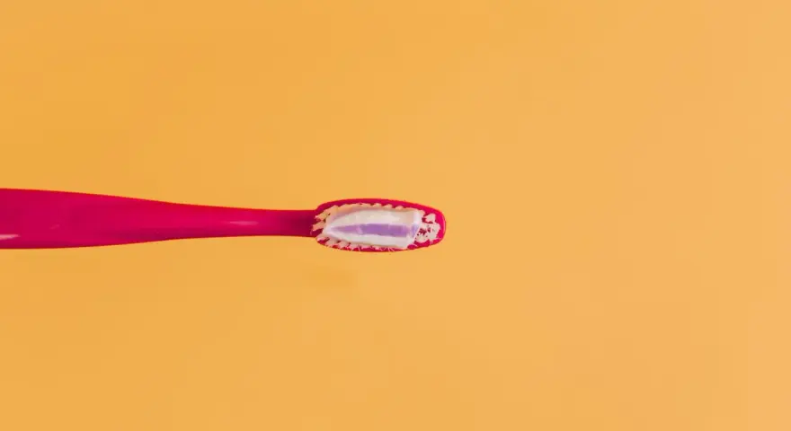 Różowa szczoteczka z pastą, która zawiera fluor. Czy fluor jest szkodliwy? Dyskusja trwa, ale pasta pomaga chronić zęby.