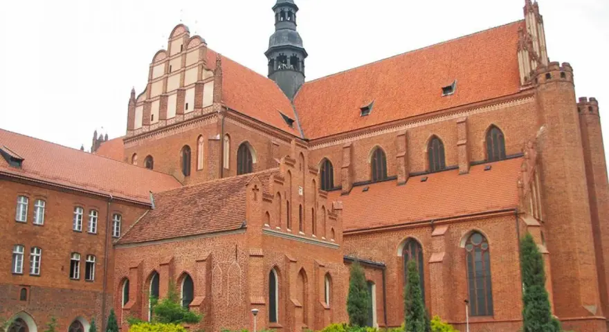 Potężny zamek krzyżacki w Pelplinie, z cegły i czerwonym dachem, góruje nad okolicą.