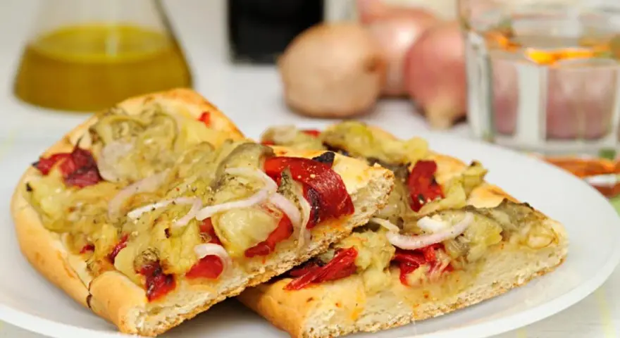 Dos porciones de coca de recapte con verduras asadas, pimientos rojos y cebolla.