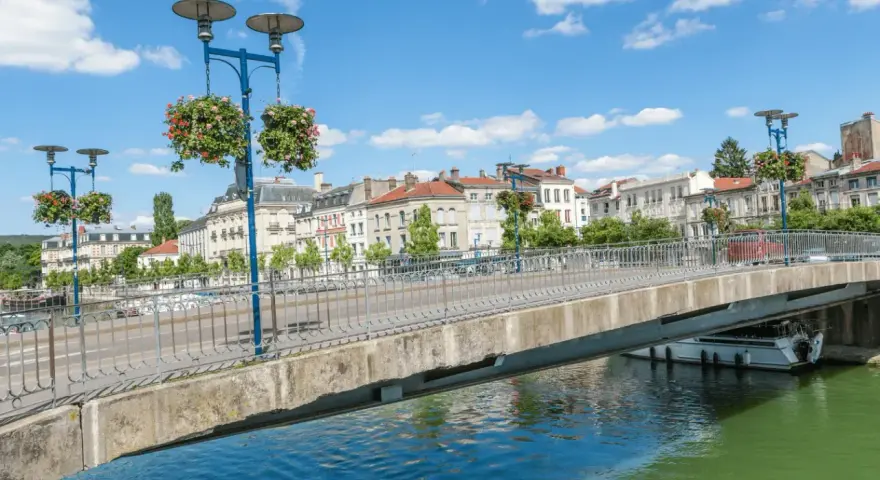 Pont fleuri sur la Meuse, une belle journée pour visiter Verdun en 1 jour. Ville historique avec des bâtiments anciens et un ciel bleu.