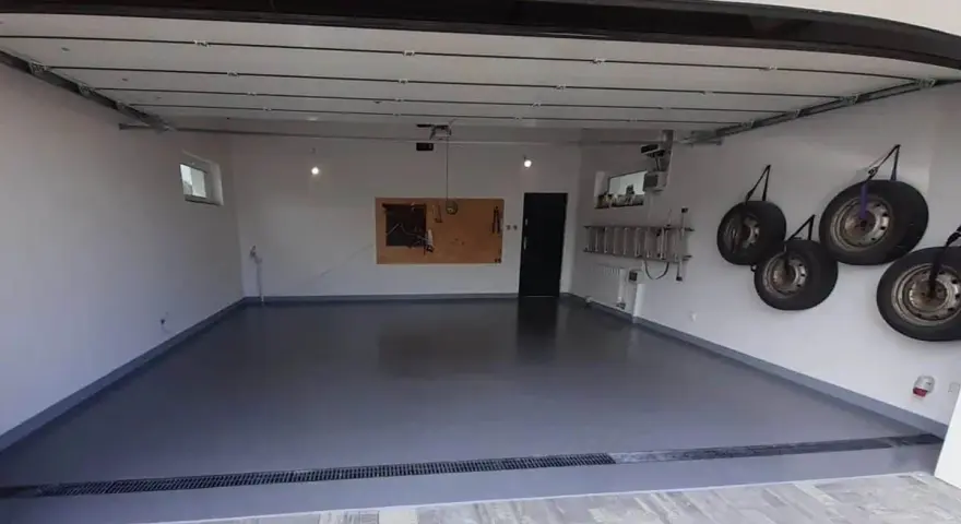 Nowa, lśniąca posadzka w garażu, cztery koła wiszące na ścianie, drabina i tablica narzędziowa.