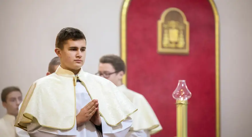 Junge Männer in festlicher Kleidung, die auf ihre Diakon Ausbildung vorbereitet werden. Sie stehen betend in einer Kirche.