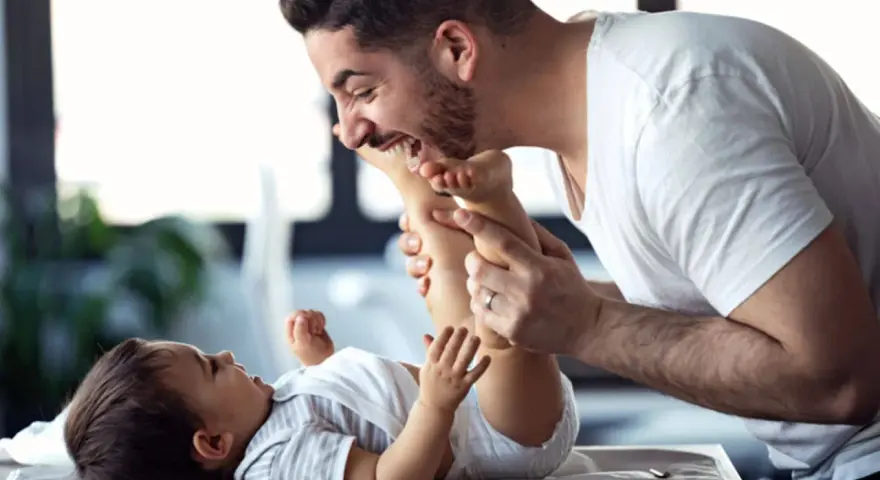 Ein lachender Vater mit Kind spielt liebevoll mit den Füßen seines Babys.