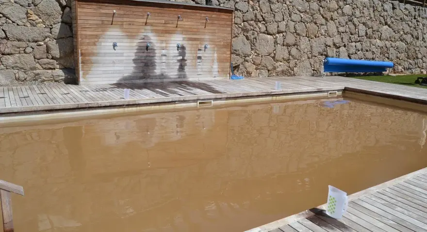 Piscina de sal con agua turbia y rodeada de madera. Al fondo, una pared de piedra y duchas.