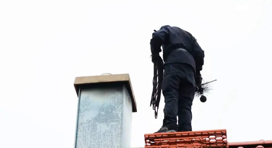 Kominiarz na dachu z narzędziami. Sprawdź, jaka jest opinia kominiarska cena za jego usługi.