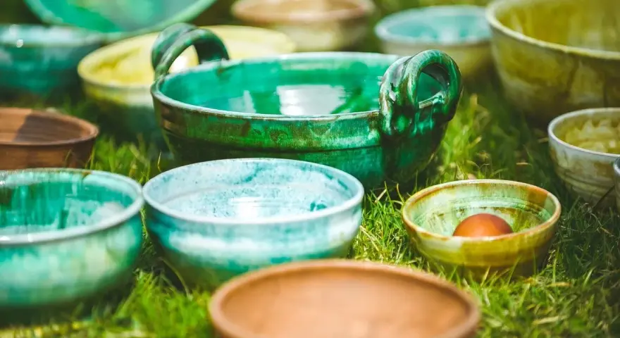 Varietà di ciotole in ceramica smaltata, che ricordano diversi tipi di argilla per modellare, disposte sull'erba.