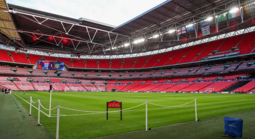 Pusta, czerwona trybuna stadionu Wembley, największego stadionu na świecie, z zieloną murawą i tabliczką "Prosimy nie wchodzić na trawę".