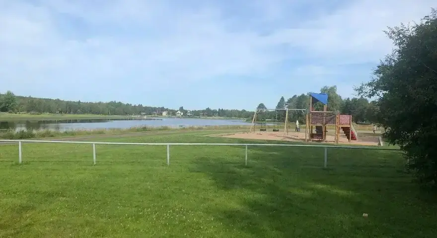 Lekplats med gungor och klätterställning vid en sjö, perfekt för familjer på Malung camping.