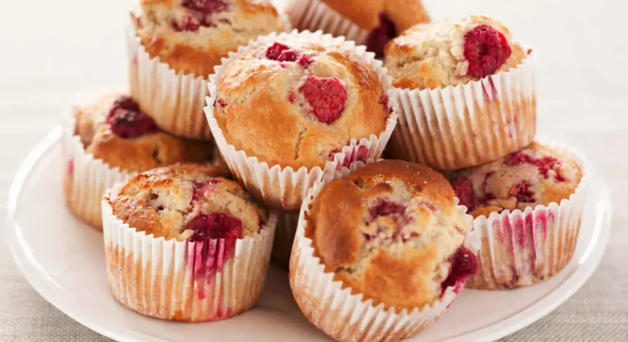 Stos muffinek z malinami na białym talerzu.