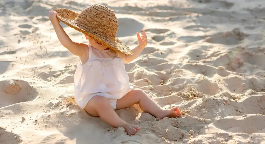 Liten bebis med stråhatt på stranden, njuter av solens värme.