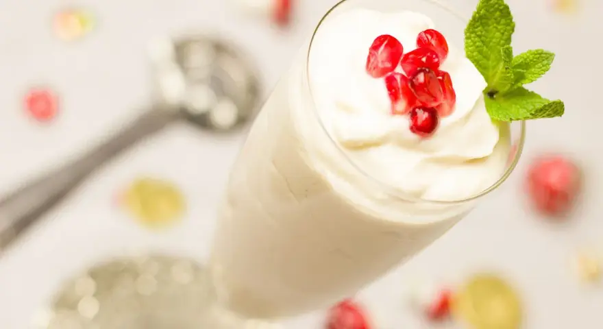 Creme double in einem Glas, garniert mit Granatapfelkernen und Minze. Ein Löffel liegt daneben.