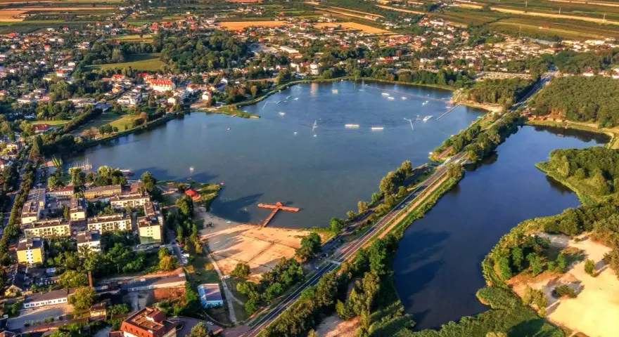 Widok z lotu ptaka na zalew Mrożyczka, z wakeboardzistami, plażą i otaczającą zielenią.
