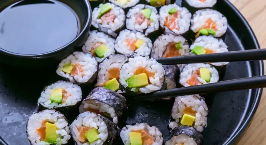 En tallrik med hemgjord sushi, perfekt för ett enkelt sushi recept. Lax och avokado rullade i ris och nori, med en skål sojasås.