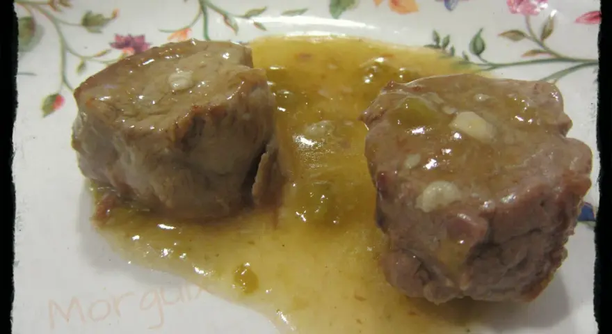 Dos trozos de solomillo al whisky en una salsa dorada, servidos en un plato con flores.
